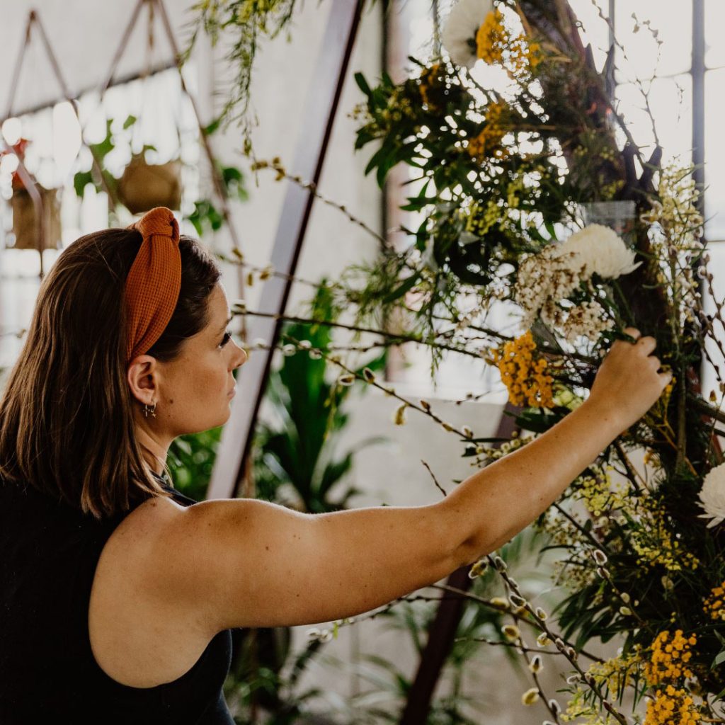 A florist (Miller Rose Botanic in Perth) attaches chicken wire and cups filled with water to an arbor using clamps, then covers them in foliage so it's a foam-free flower arrangement