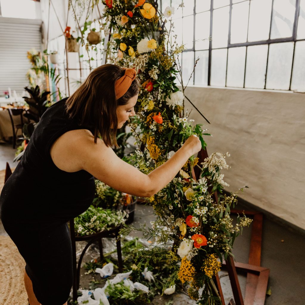 A florist (Miller Rose Botanic in Perth) attaches chicken wire and cups filled with water to an arbor using clamps, then covers them in foliage so it's a foam-free flower arrangement