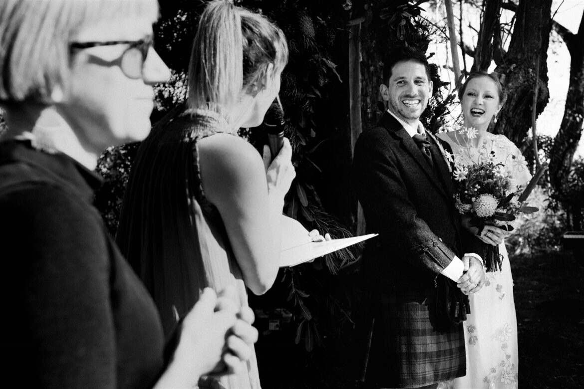 A groom wearing a kilt and a bride wearing a vintage wedding dress both read their vows to each other in their wedding ceremony in the Blue Mountains, with an Auslan interpreter