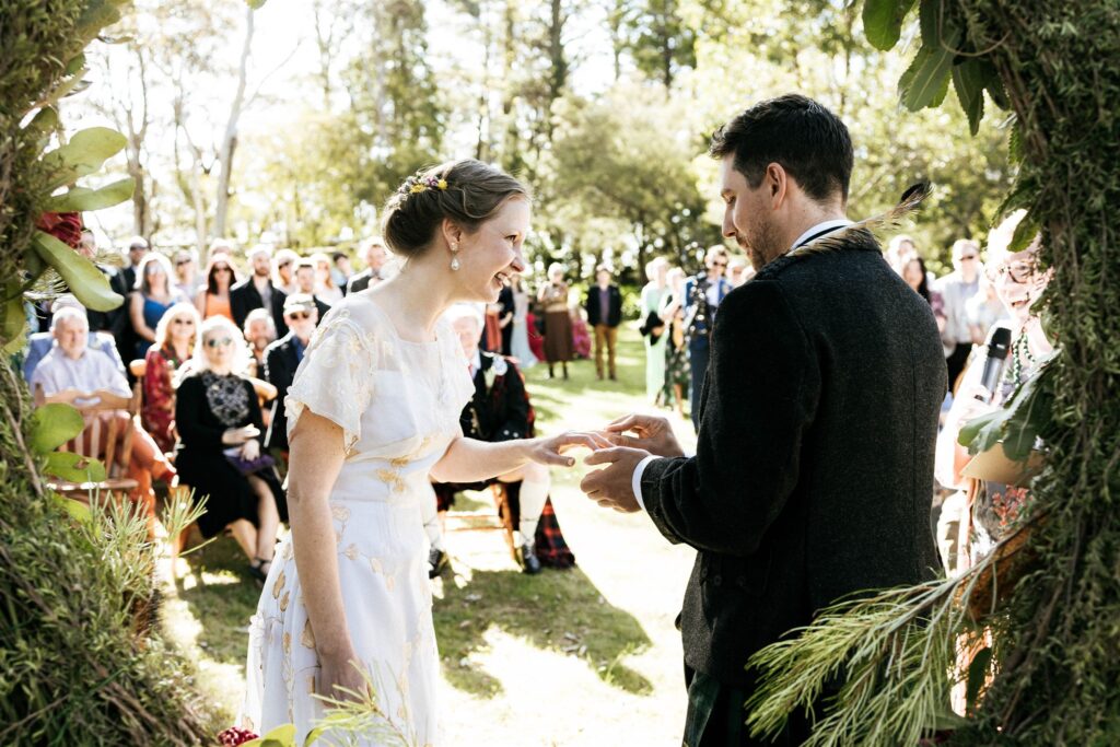 A groom wearing a kilt and a bride wearing a vintage wedding dress both read their vows to each other in their wedding ceremony in the Blue Mountains