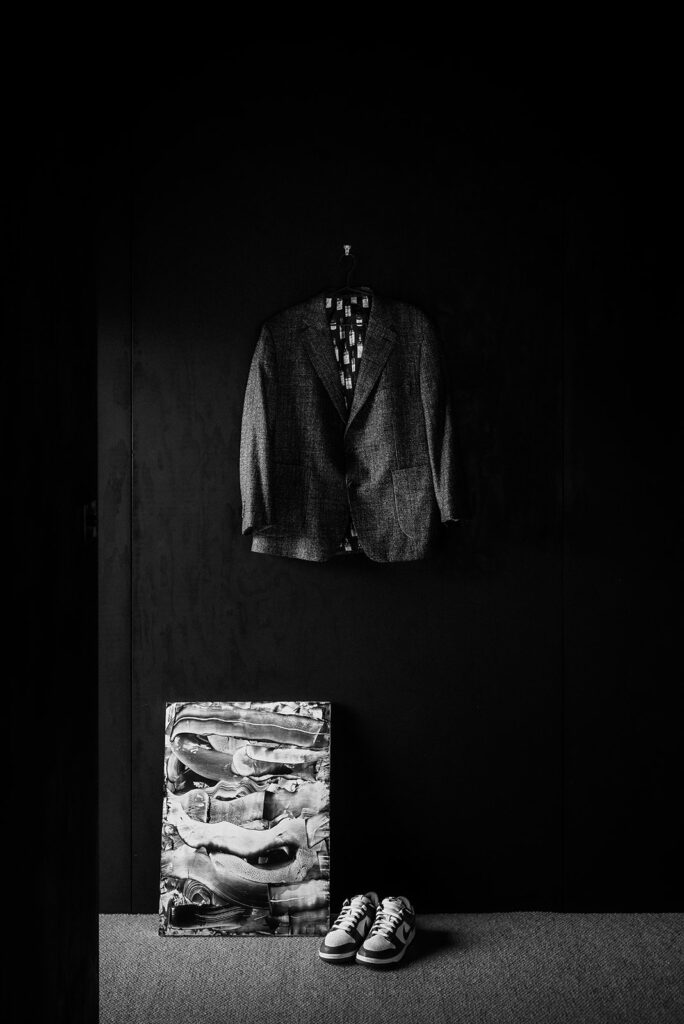 A suit hangs from a wall along with a pair of Nike sneakers and some art leaning against the wall.