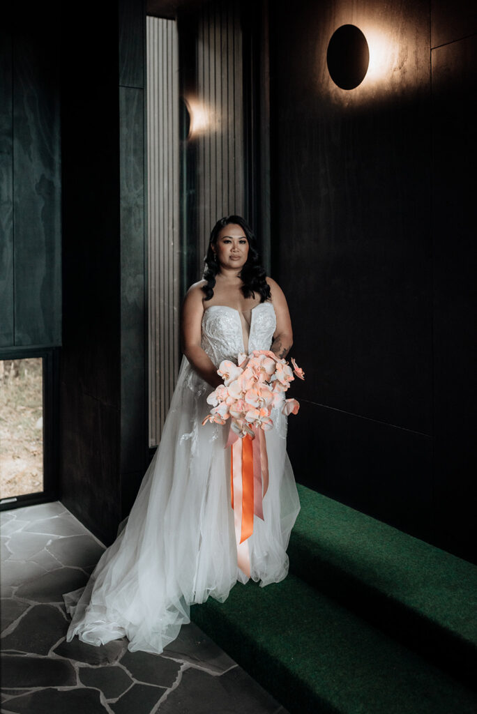 A bride is dressed glamorously with hollywood curls and a white dress and veil. She holds beautiful flowers and is wearing Nike sneakers under her dress. She is waiting to get married at an intimate elopement at their Airbnb in Hobart, Tasmania.