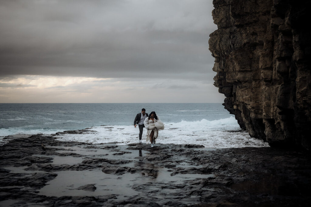 A bride and groom hold hands on a stormy coastline of Hobart, Tasmania
