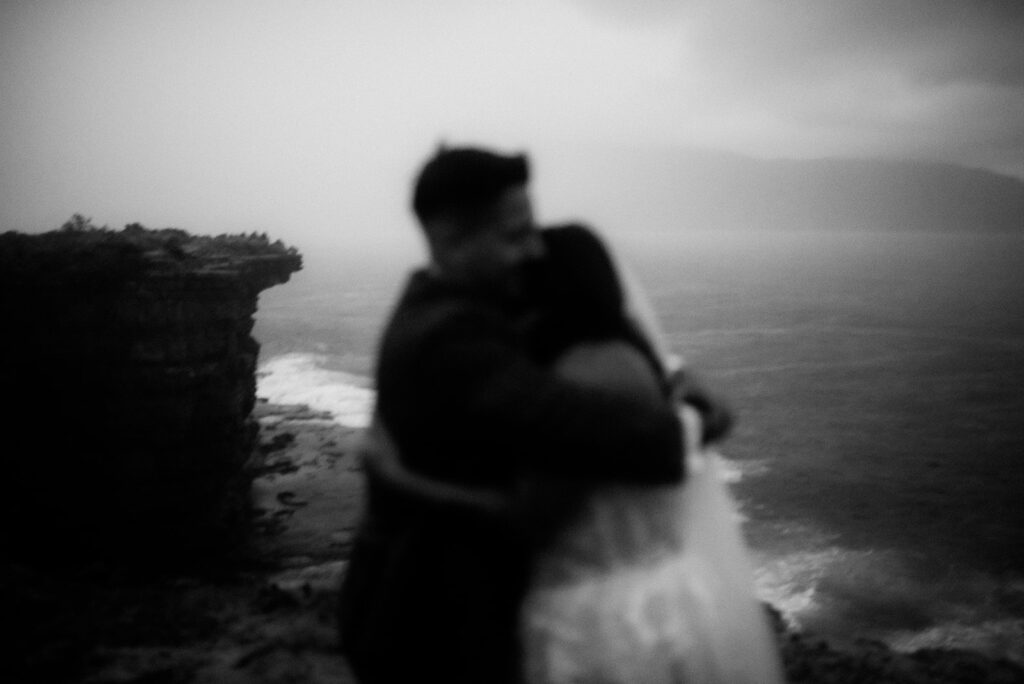 A bride and groom embrace on a stormy coastline of Hobart, Tasmania