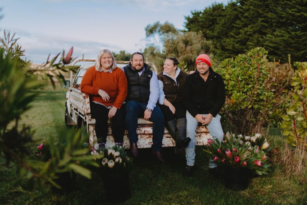 Nikki Davey and her team are sitting on the back of a ute at a flower farm