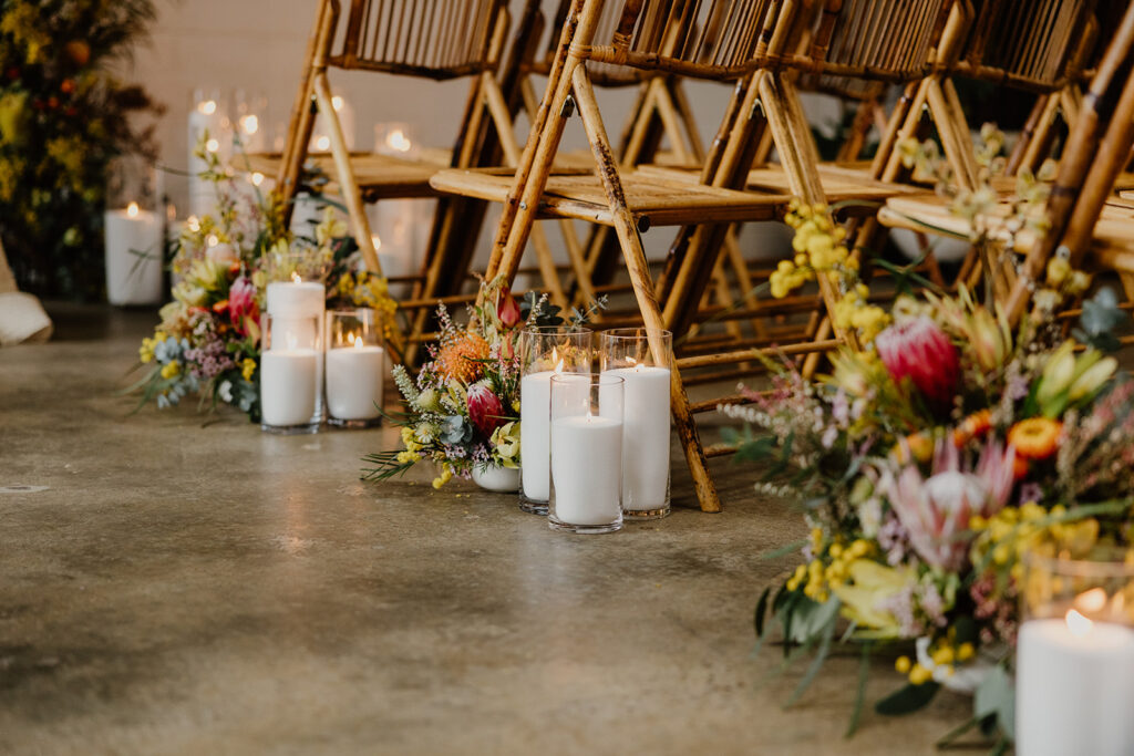 Candles made from granulated wax sit in a glass vessel next to native flowers as a sustainable decoration for a wedding